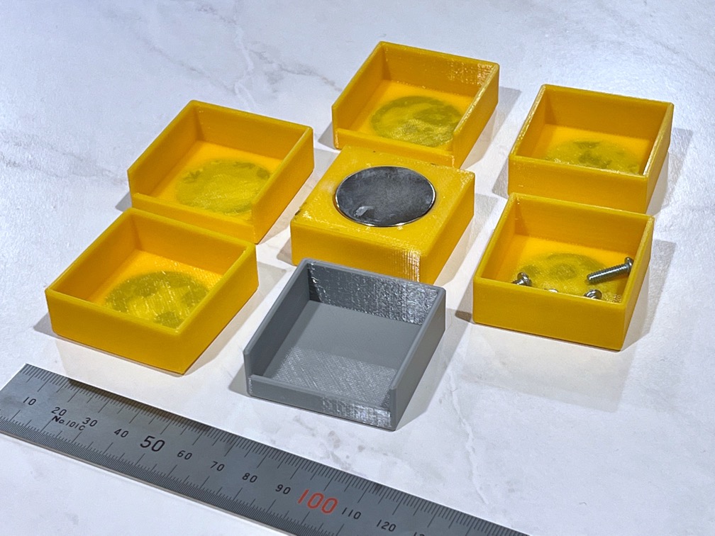 Seven small trays, 3D-printed in yellow and gray plastic